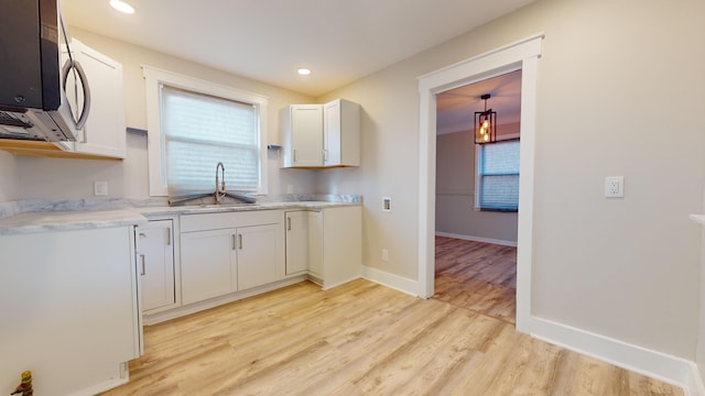 kitchen featuring light countertops, a sink, stainless steel microwave, baseboards, and light wood-style floors