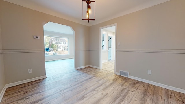 empty room featuring baseboards, visible vents, arched walkways, and light wood-style floors