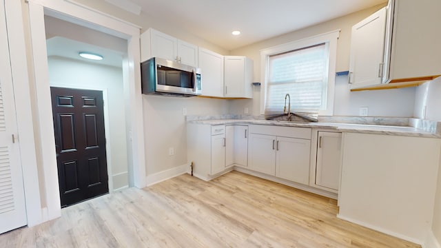 kitchen featuring light wood-type flooring, stainless steel microwave, baseboards, a sink, and white cabinets