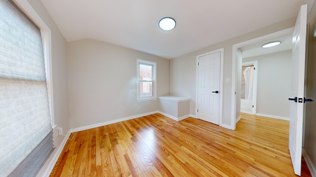 empty room with vaulted ceiling, baseboards, and light wood finished floors
