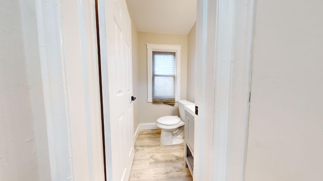 half bath with toilet, wood finished floors, vanity, and baseboards