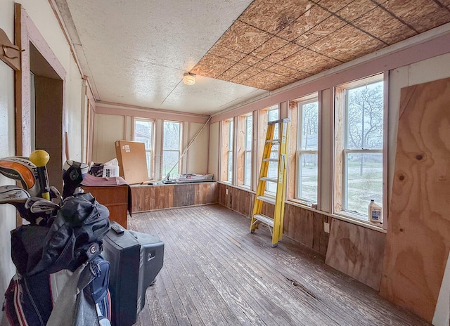 sunroom / solarium with wood-type flooring, an ornate ceiling, wood walls, and a wealth of natural light