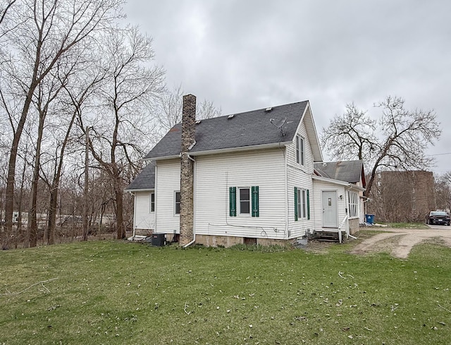 back of property with a lawn, entry steps, central AC, a shingled roof, and a chimney