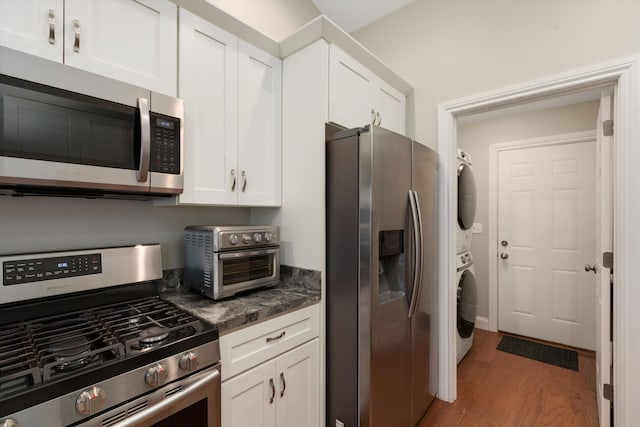 33172 Swallow Dr, Rockwood, MI 48173 - kitchen featuring dark countertops, white cabinetry, light wood-style flooring, appliances with stainless steel finishes, and stacked washer and clothes dryer
