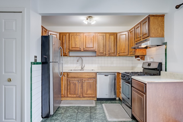 kitchen with light countertops, tasteful backsplash, under cabinet range hood, a sink, and appliances with stainless steel finishes