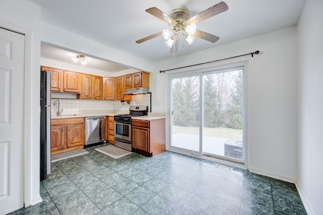 kitchen with light countertops, a sink, backsplash, stainless steel appliances, and ceiling fan