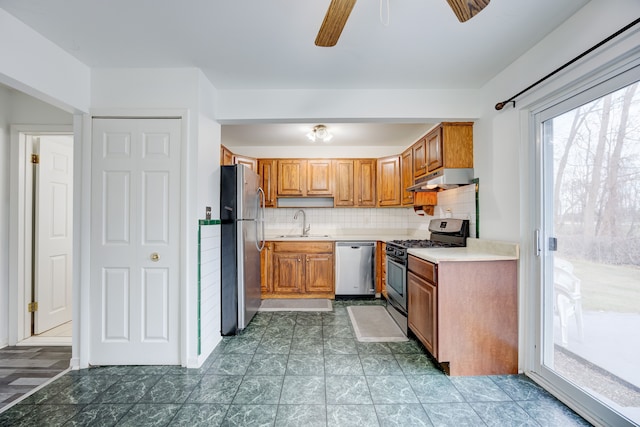 kitchen with backsplash, a ceiling fan, appliances with stainless steel finishes, brown cabinets, and under cabinet range hood