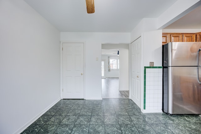 kitchen featuring brown cabinets, a ceiling fan, baseboards, and freestanding refrigerator
