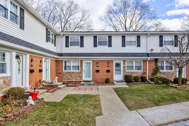 view of property featuring a shingled roof, a front yard, stone siding, and brick siding