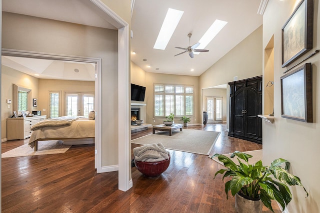 foyer with a lit fireplace, high vaulted ceiling, a skylight, baseboards, and hardwood / wood-style floors