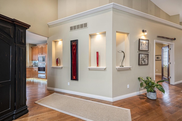 corridor with baseboards, visible vents, a high ceiling, and wood-type flooring