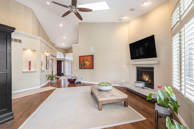 living room with a warm lit fireplace, visible vents, wood finished floors, and ceiling fan
