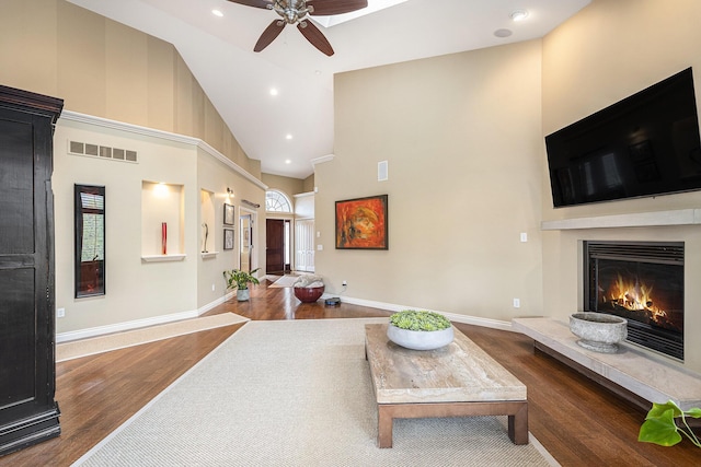 living room with a warm lit fireplace, visible vents, baseboards, ceiling fan, and wood finished floors