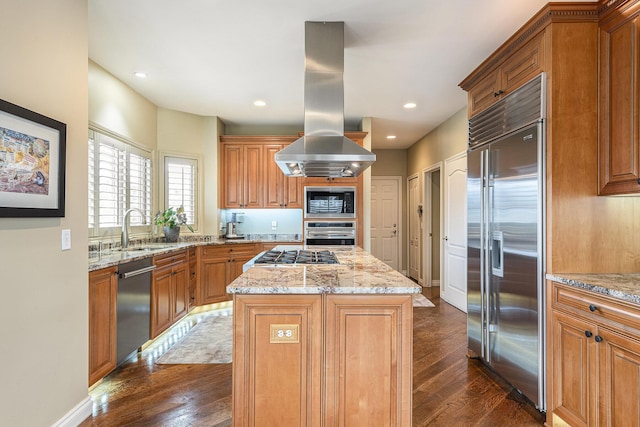 kitchen with dark wood-style flooring, island exhaust hood, a kitchen island, a sink, and built in appliances