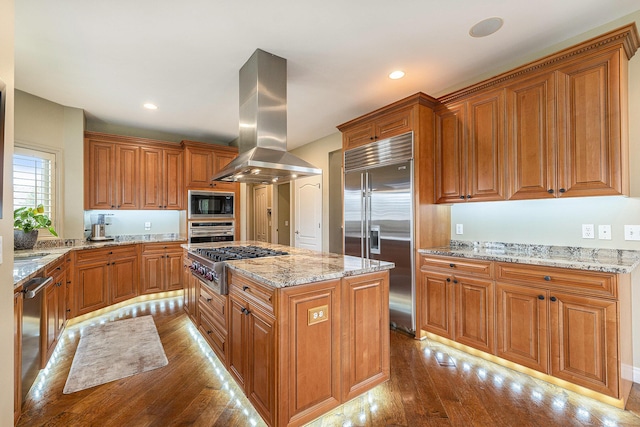 kitchen featuring light stone counters, a kitchen island, built in appliances, island exhaust hood, and hardwood / wood-style floors
