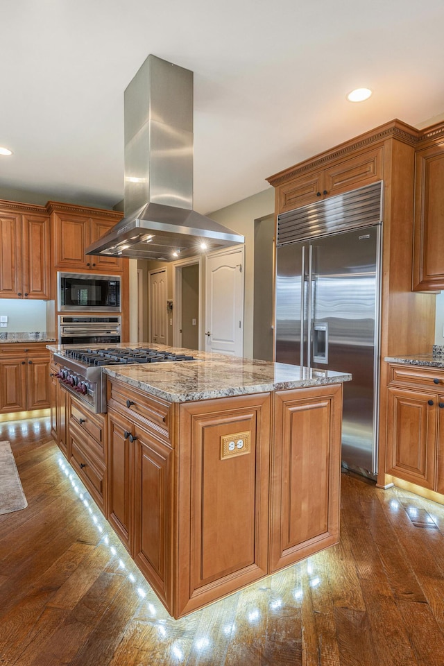 kitchen with a center island, island exhaust hood, dark wood-style floors, built in appliances, and brown cabinetry