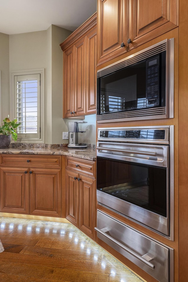 kitchen featuring a warming drawer, oven, built in microwave, light stone countertops, and brown cabinetry