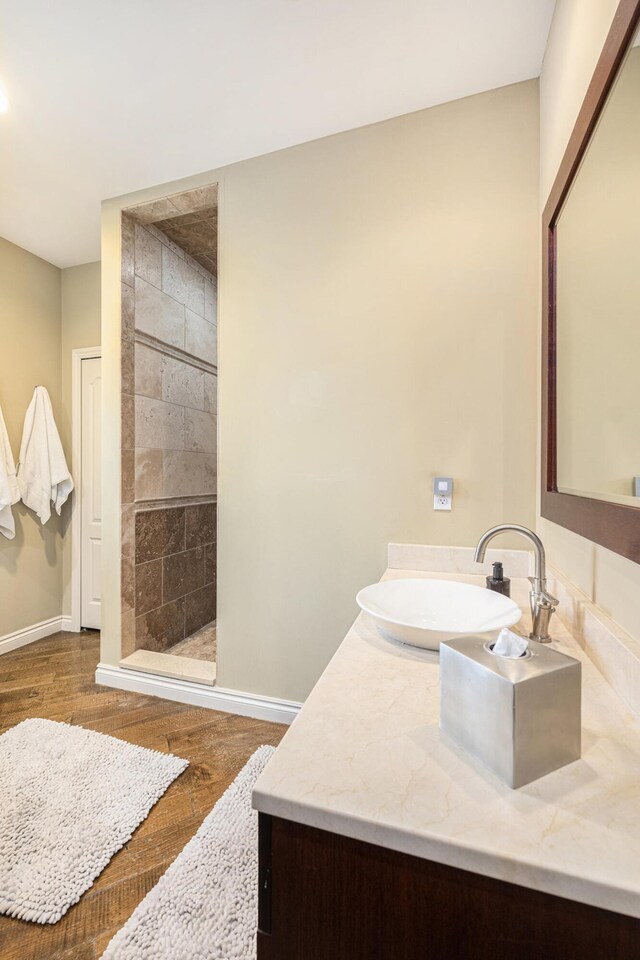 bathroom featuring wood finished floors, vanity, baseboards, and a walk in shower