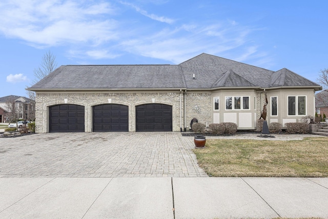 view of front facade featuring decorative driveway, a garage, a front yard, brick siding, and a shingled roof