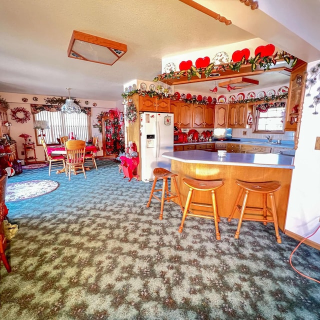 kitchen featuring white fridge with ice dispenser, brown cabinetry, a peninsula, a breakfast bar, and carpet floors