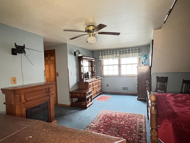 bedroom with ceiling fan, a textured ceiling, a glass covered fireplace, carpet floors, and baseboards