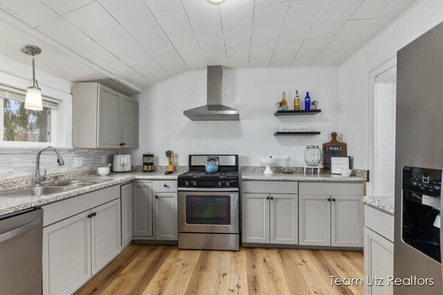 kitchen featuring appliances with stainless steel finishes, a sink, light wood-style floors, gray cabinetry, and wall chimney range hood
