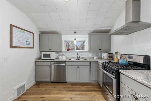 kitchen with a sink, appliances with stainless steel finishes, gray cabinetry, and wall chimney exhaust hood