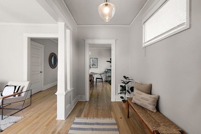 hallway featuring ornate columns, light wood-style flooring, crown molding, and baseboards