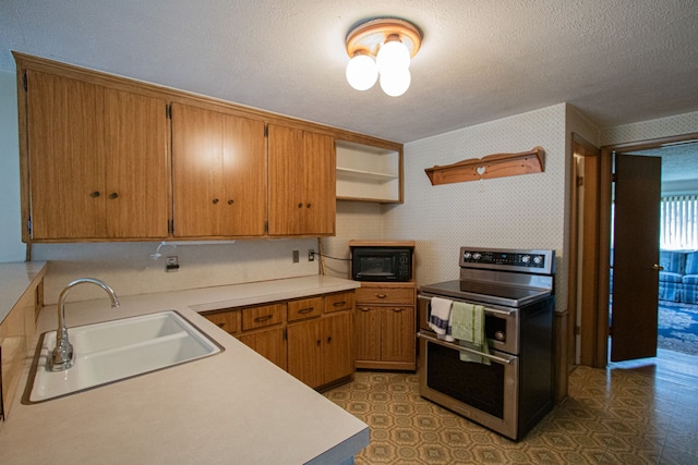 kitchen featuring tile patterned floors, a sink, double oven range, a textured ceiling, and wallpapered walls