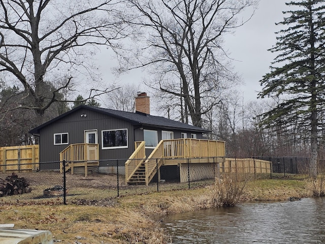 rear view of property featuring a deck with water view, fence, and a chimney