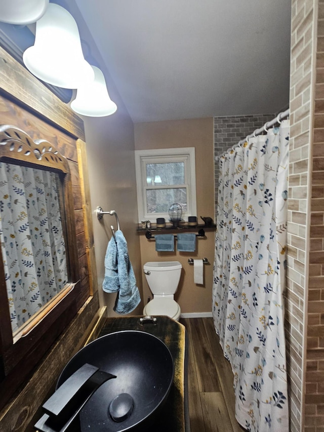 bathroom with baseboards, wood finished floors, toilet, curtained shower, and a sink