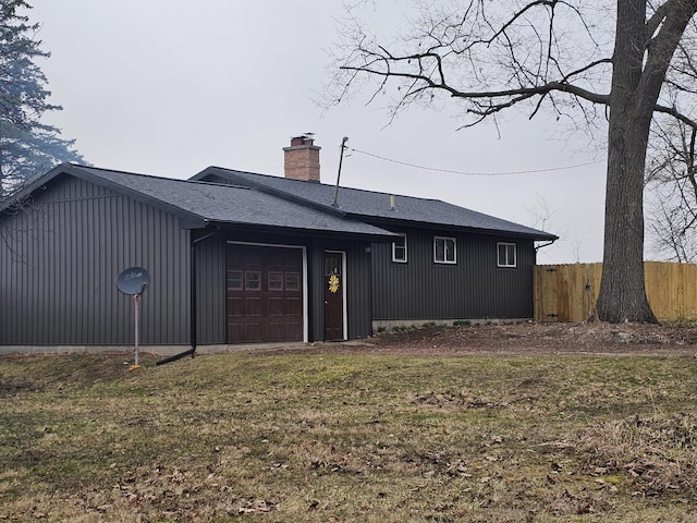 back of house featuring an attached garage, a chimney, fence, and roof with shingles