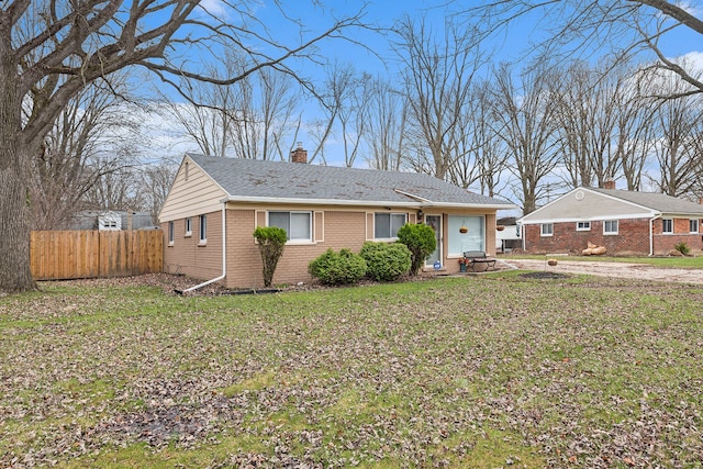 ranch-style house with a chimney, a front yard, fence, and brick siding