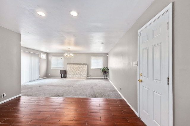 unfurnished living room with baseboards, wood finished floors, a chandelier, and carpet