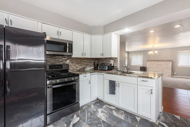 kitchen with decorative backsplash, a chandelier, a peninsula, stainless steel appliances, and a sink
