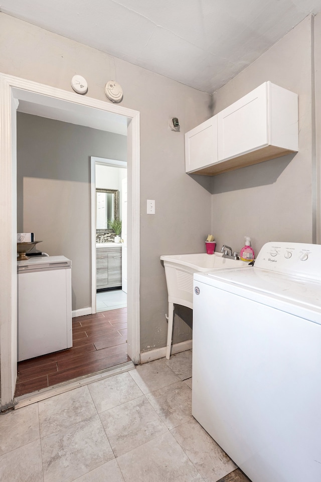clothes washing area with a sink, cabinet space, washer / dryer, and baseboards