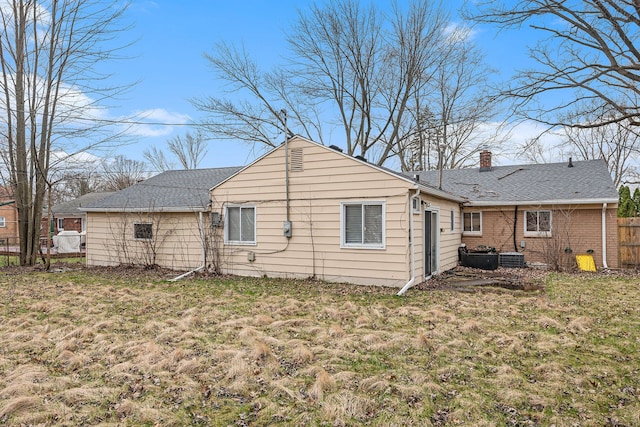 back of property with a lawn, a chimney, fence, and roof with shingles