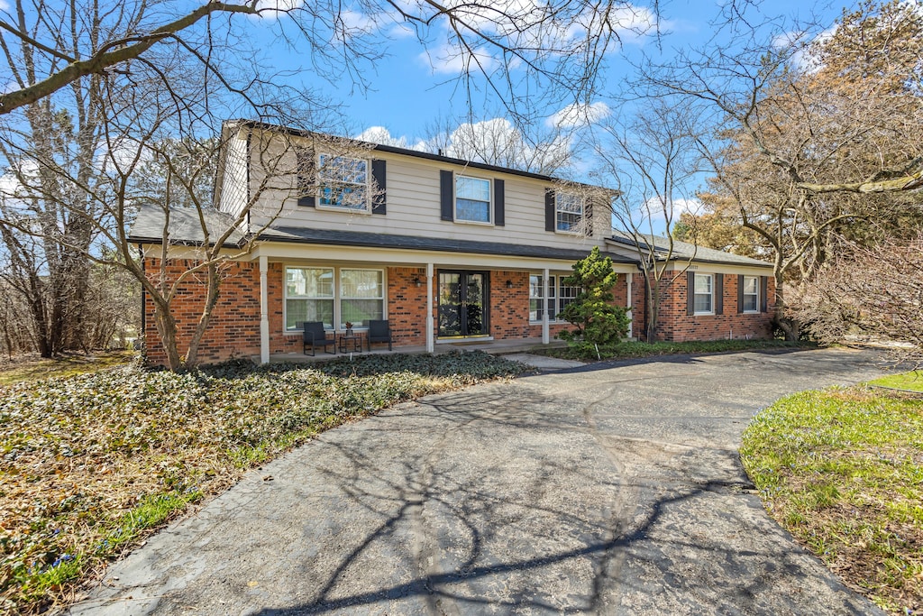 traditional-style house featuring a porch, driveway, and brick siding