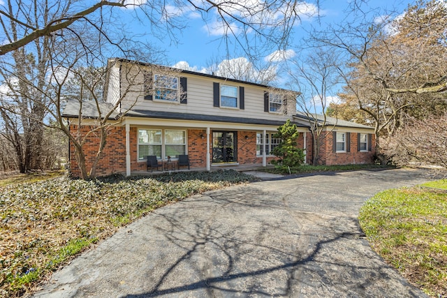 traditional-style house featuring a porch, driveway, and brick siding