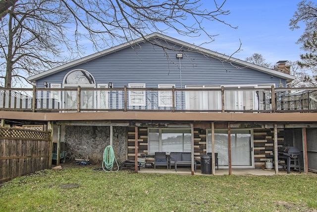 rear view of house with stone siding, a chimney, a deck, a patio, and a lawn
