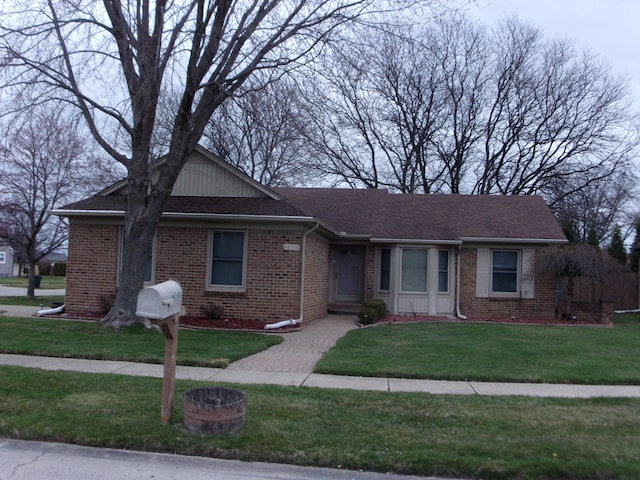 single story home featuring a shingled roof, a front yard, and brick siding