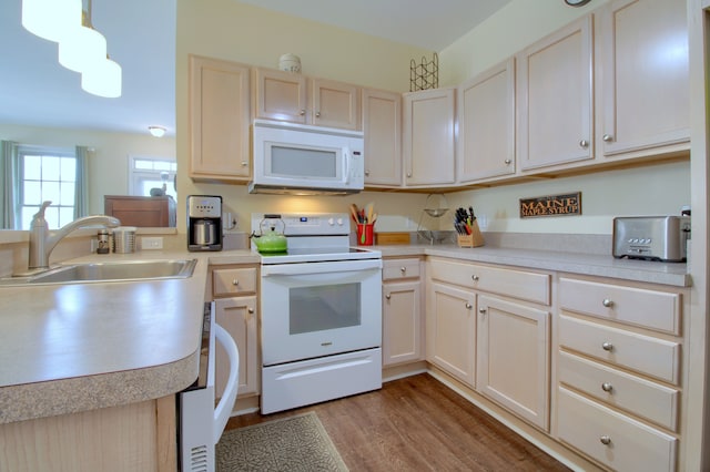 kitchen with a sink, light countertops, wood finished floors, white appliances, and a peninsula