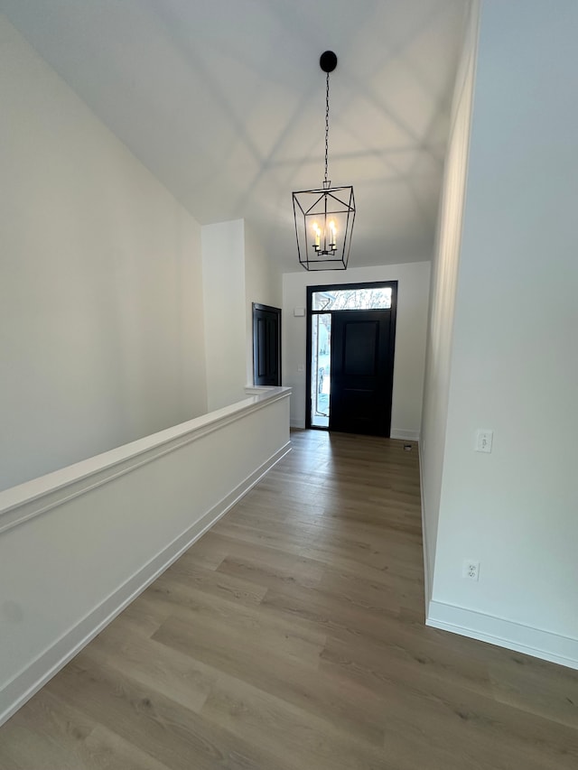 doorway to outside with wood finished floors, lofted ceiling, baseboards, and an inviting chandelier