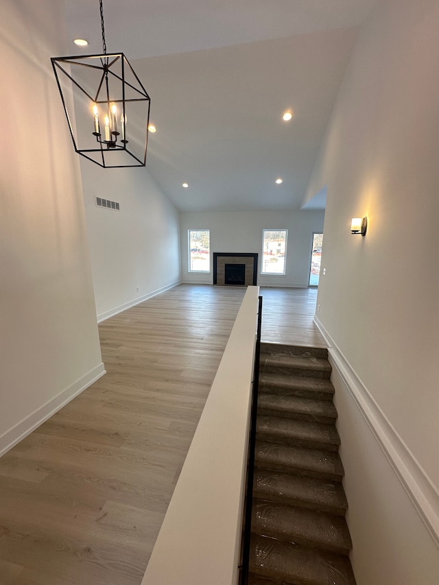 stairs featuring a notable chandelier, lofted ceiling, visible vents, and wood finished floors
