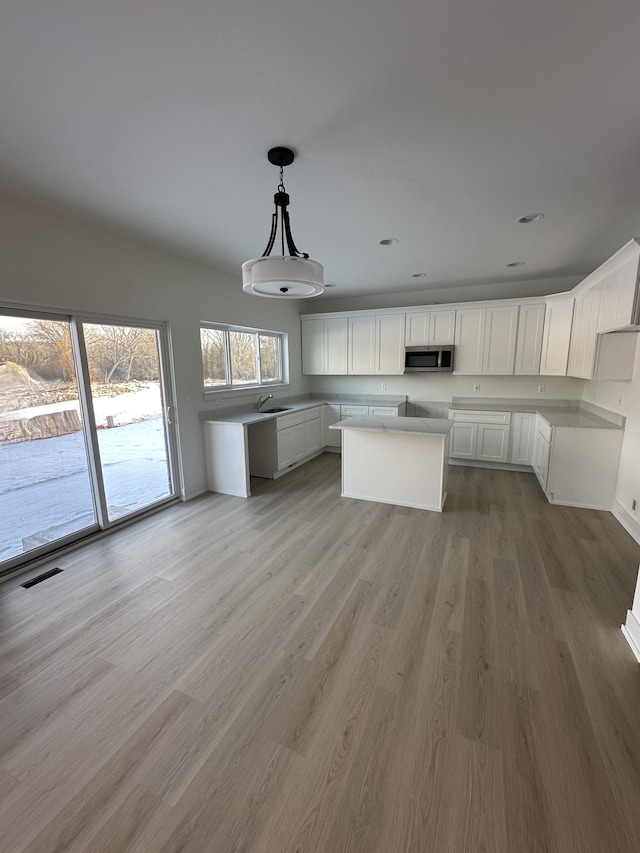kitchen with a sink, light wood-style flooring, stainless steel microwave, white cabinetry, and visible vents