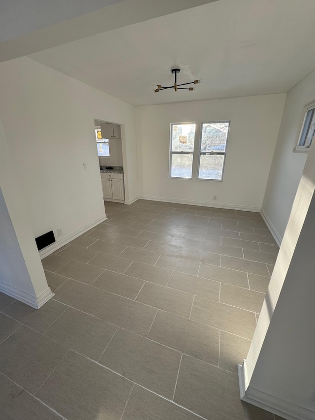 spare room featuring baseboards and a notable chandelier