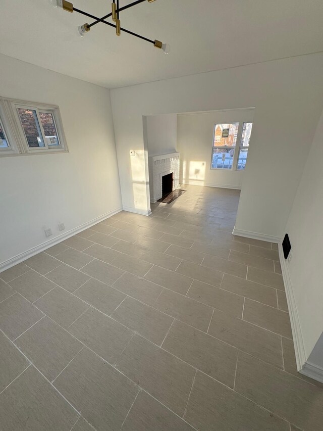unfurnished living room featuring an inviting chandelier, baseboards, and a fireplace