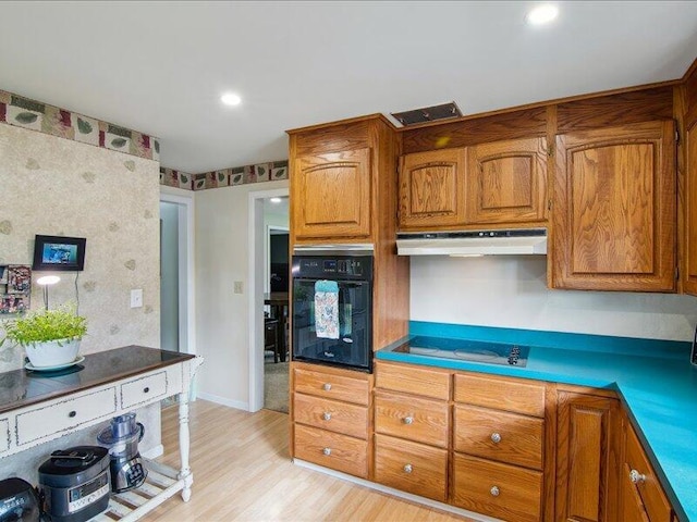 kitchen featuring light wood-type flooring, brown cabinetry, under cabinet range hood, visible vents, and black appliances