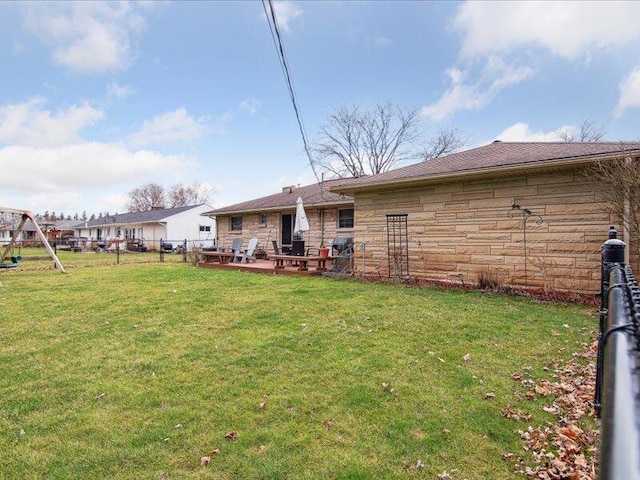 rear view of property with fence, a lawn, stone siding, and a playground