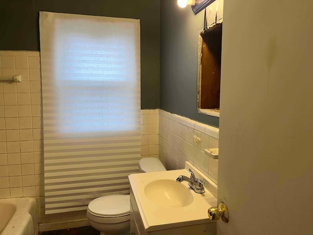 bathroom with a washtub, tile walls, a wainscoted wall, vanity, and toilet